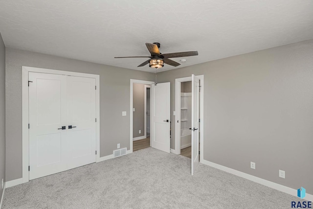 unfurnished bedroom featuring ceiling fan, a closet, light carpet, and a textured ceiling