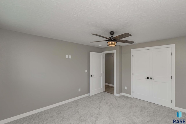 unfurnished bedroom with a textured ceiling, light colored carpet, a closet, and ceiling fan