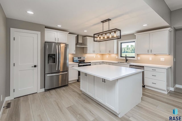 kitchen with sink, decorative light fixtures, wall chimney range hood, stainless steel appliances, and white cabinets