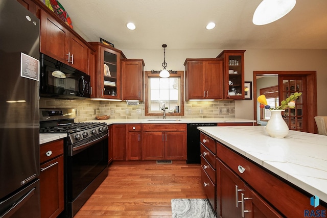 kitchen with sink, hanging light fixtures, light hardwood / wood-style floors, decorative backsplash, and black appliances