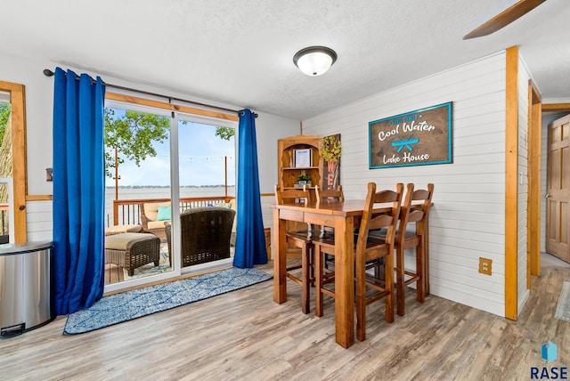 dining area with hardwood / wood-style flooring, a water view, a textured ceiling, and wood walls