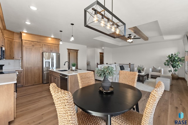 dining area featuring ceiling fan, a tray ceiling, sink, and light hardwood / wood-style flooring