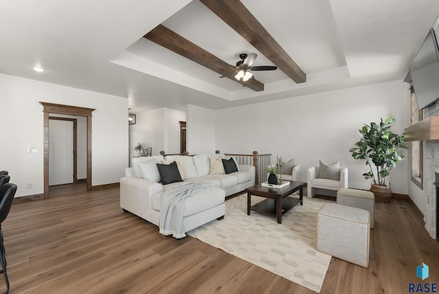 living room featuring hardwood / wood-style flooring, a raised ceiling, a stone fireplace, and beamed ceiling