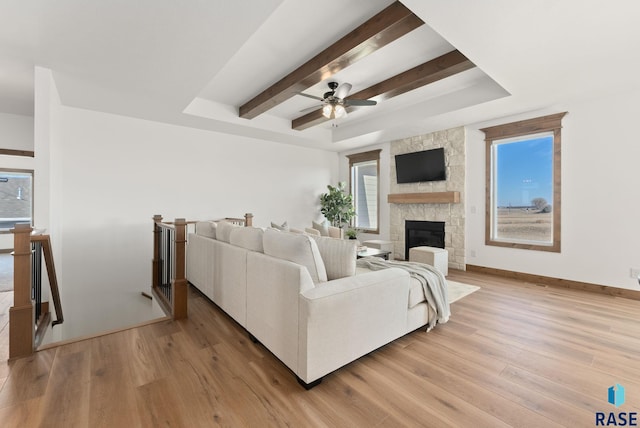 living room featuring beam ceiling, ceiling fan, a fireplace, and light hardwood / wood-style flooring