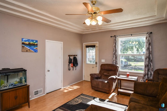 living room featuring a raised ceiling, ceiling fan, a textured ceiling, and light hardwood / wood-style floors