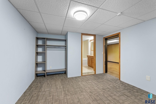 unfurnished bedroom featuring carpet flooring, a drop ceiling, ensuite bath, and a closet