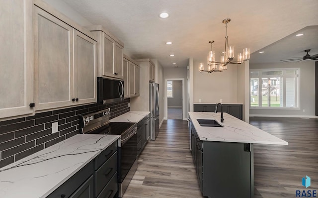 kitchen with decorative light fixtures, an island with sink, sink, decorative backsplash, and stainless steel appliances