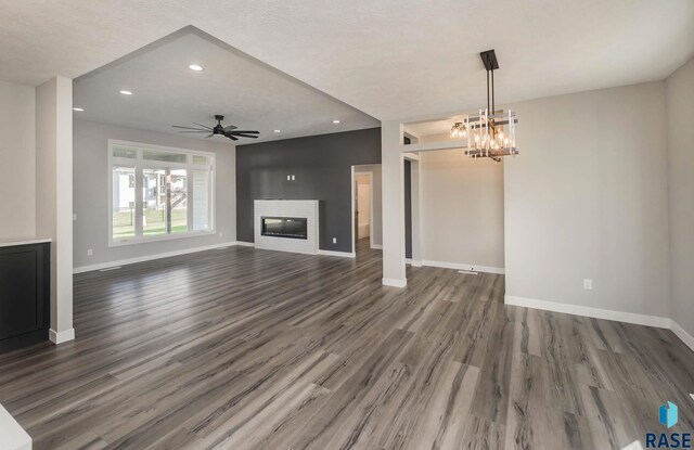 unfurnished living room with dark hardwood / wood-style flooring and ceiling fan with notable chandelier