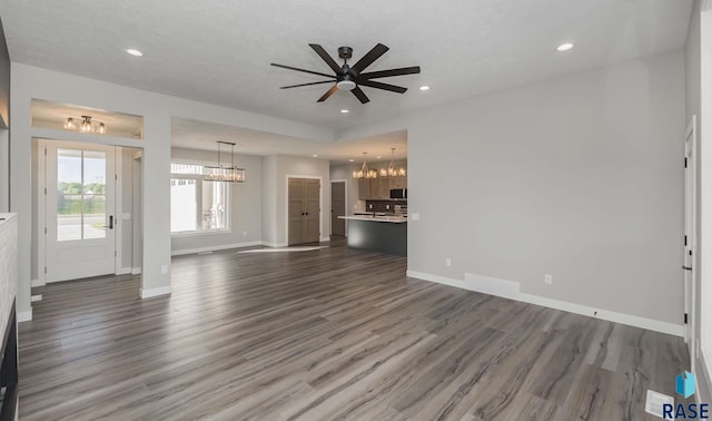 unfurnished living room with dark hardwood / wood-style floors, ceiling fan with notable chandelier, and a textured ceiling