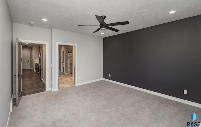 unfurnished bedroom featuring ceiling fan, ensuite bathroom, a textured ceiling, and dark carpet