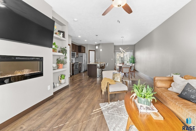 living room featuring built in shelves, ceiling fan, dark hardwood / wood-style floors, and sink