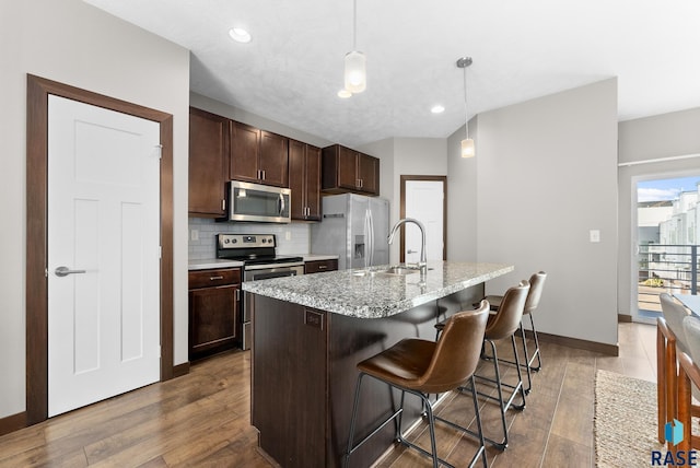 kitchen featuring sink, a breakfast bar, appliances with stainless steel finishes, a kitchen island with sink, and decorative light fixtures