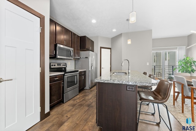 kitchen with a breakfast bar, sink, decorative light fixtures, appliances with stainless steel finishes, and a kitchen island with sink