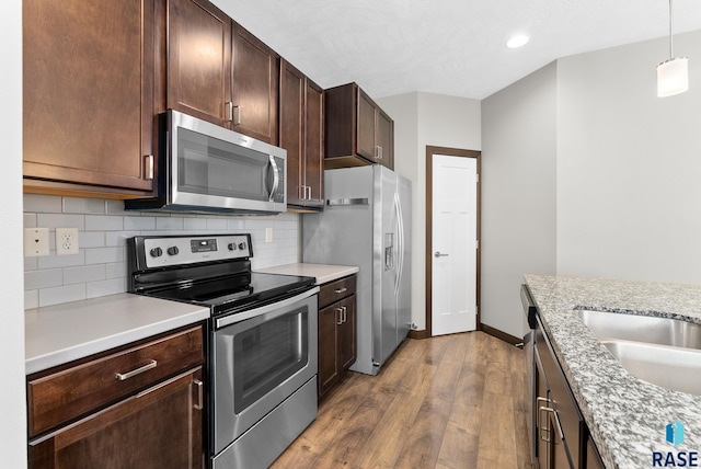 kitchen with hardwood / wood-style floors, decorative light fixtures, light stone countertops, and appliances with stainless steel finishes