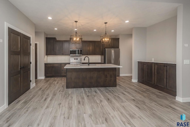 kitchen with sink, appliances with stainless steel finishes, hanging light fixtures, dark brown cabinetry, and a center island with sink