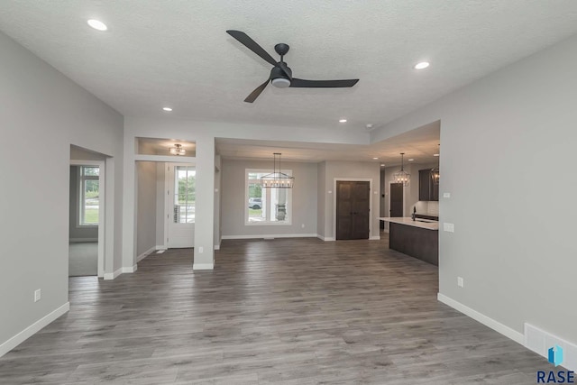 unfurnished living room featuring sink, hardwood / wood-style flooring, ceiling fan with notable chandelier, and a textured ceiling