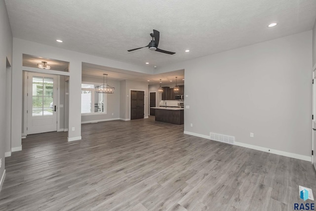 unfurnished living room featuring hardwood / wood-style flooring, ceiling fan with notable chandelier, and a textured ceiling