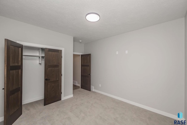 unfurnished bedroom featuring light carpet, a closet, and a textured ceiling