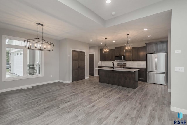 kitchen featuring appliances with stainless steel finishes, a kitchen island with sink, hanging light fixtures, dark brown cabinetry, and decorative backsplash