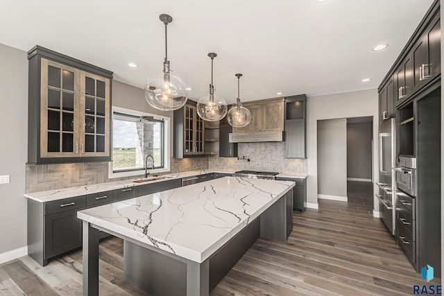 kitchen with sink, backsplash, a center island, light stone counters, and decorative light fixtures