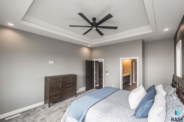 carpeted bedroom featuring ensuite bath, ceiling fan, and a tray ceiling