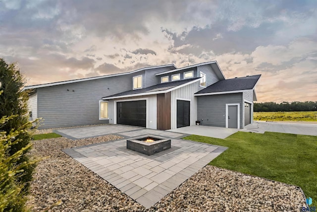 back house at dusk featuring a garage, a yard, a patio area, and a fire pit