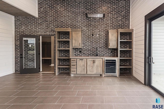 wine room with wine cooler, tile patterned floors, sink, wood walls, and brick wall