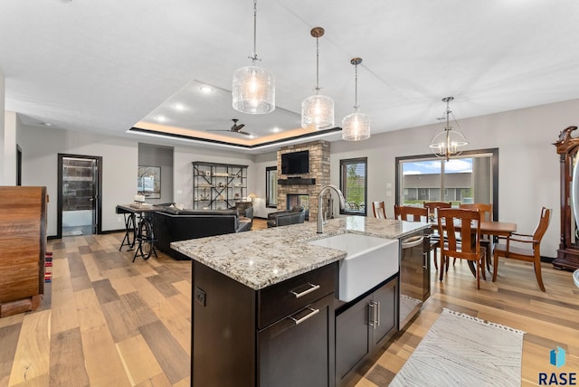 kitchen with sink, hanging light fixtures, a center island with sink, stainless steel dishwasher, and a fireplace