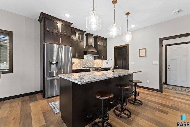 kitchen featuring dark brown cabinetry, custom exhaust hood, an island with sink, pendant lighting, and stainless steel appliances