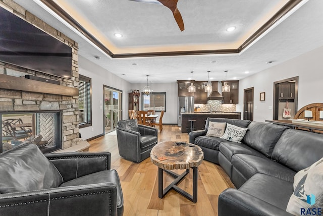 living room with a chandelier, a fireplace, a raised ceiling, and light hardwood / wood-style floors