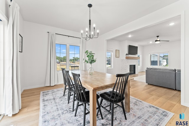 dining area with a brick fireplace, ceiling fan with notable chandelier, and light hardwood / wood-style flooring