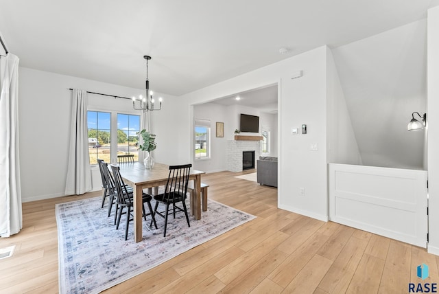 dining space with an inviting chandelier, a fireplace, and light wood-type flooring