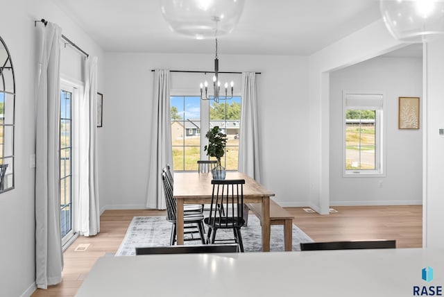 dining area featuring a healthy amount of sunlight, light hardwood / wood-style flooring, and a notable chandelier