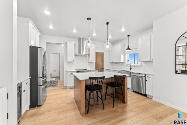 kitchen with wall chimney range hood, a center island, white cabinets, and appliances with stainless steel finishes