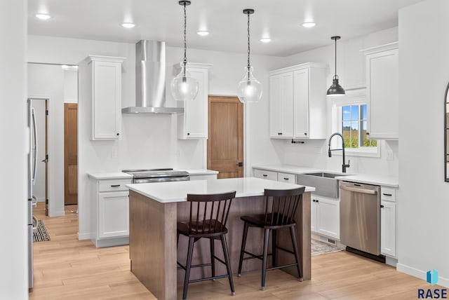 kitchen with wall chimney range hood, sink, stainless steel appliances, white cabinets, and a kitchen island