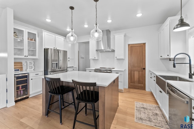 kitchen with a kitchen island, appliances with stainless steel finishes, white cabinetry, wine cooler, and wall chimney range hood