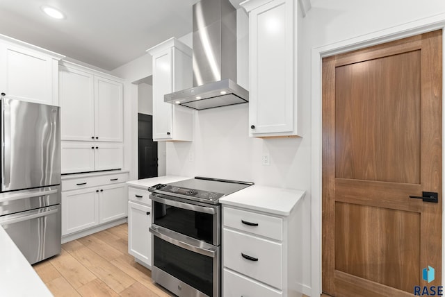 kitchen featuring white cabinets, appliances with stainless steel finishes, light wood-type flooring, and wall chimney range hood