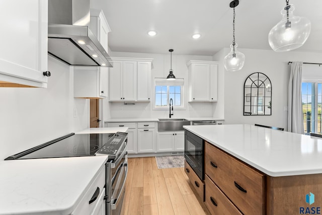 kitchen with sink, decorative light fixtures, black microwave, white cabinets, and wall chimney range hood