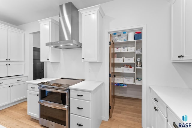 kitchen with white cabinetry, double oven range, light hardwood / wood-style flooring, and wall chimney range hood