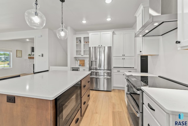 kitchen featuring appliances with stainless steel finishes, pendant lighting, white cabinets, a center island, and wall chimney range hood