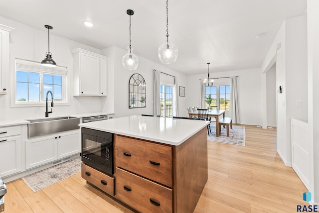 kitchen with black microwave, sink, white cabinets, a center island, and light hardwood / wood-style flooring