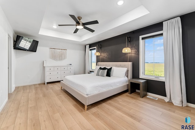 bedroom featuring a tray ceiling, light hardwood / wood-style floors, and ceiling fan