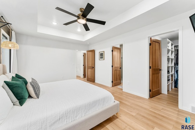 bedroom featuring a raised ceiling, ceiling fan, and light hardwood / wood-style flooring