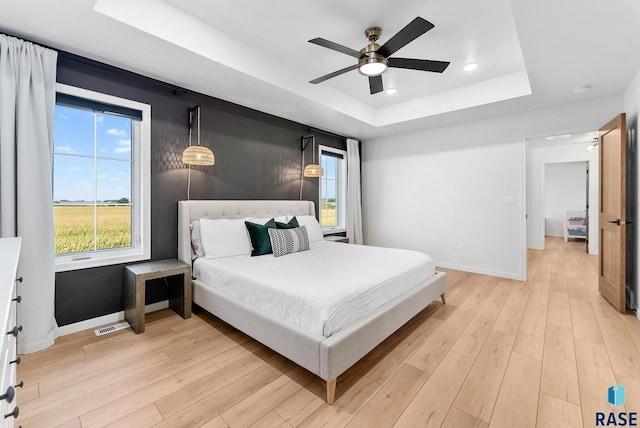 bedroom with a tray ceiling, ceiling fan, and light wood-type flooring