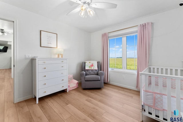 bedroom featuring ceiling fan, light hardwood / wood-style flooring, and a crib