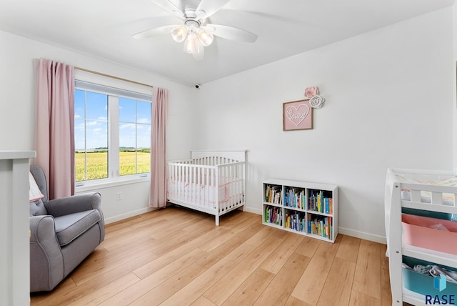 bedroom featuring a nursery area, ceiling fan, and light wood-type flooring