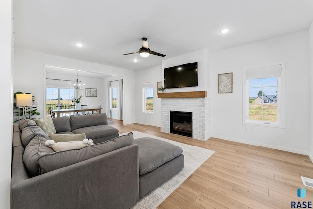 living room with a brick fireplace, ceiling fan with notable chandelier, and light hardwood / wood-style flooring