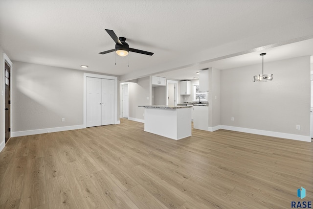 unfurnished living room with ceiling fan with notable chandelier, light hardwood / wood-style flooring, and a textured ceiling