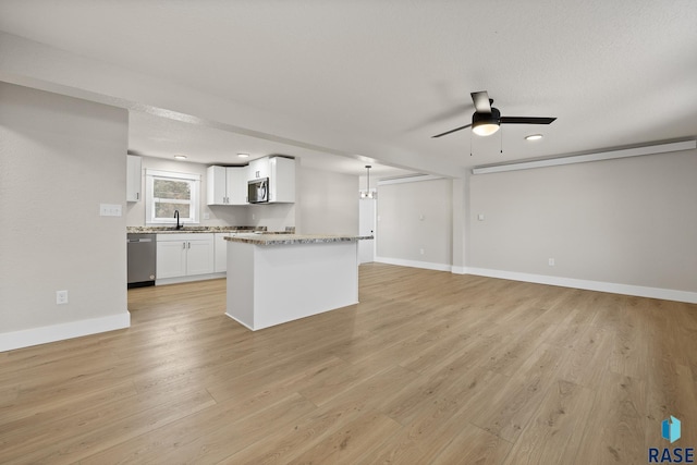 kitchen with white cabinetry, light stone counters, hanging light fixtures, light wood-type flooring, and appliances with stainless steel finishes