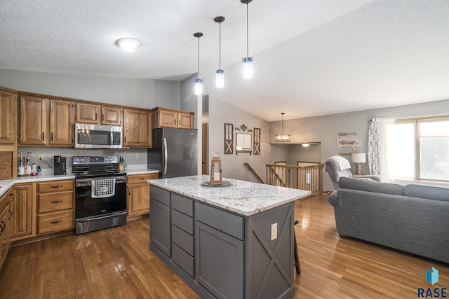 kitchen with dark wood-type flooring, a center island, hanging light fixtures, appliances with stainless steel finishes, and light stone countertops